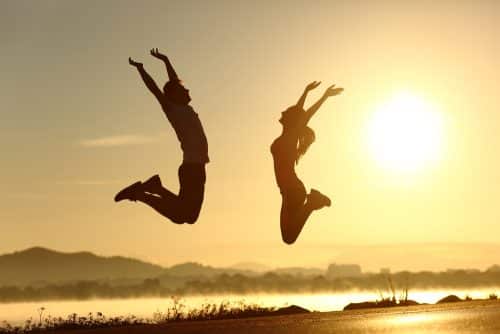 two people jumping into the air in front of the sun.