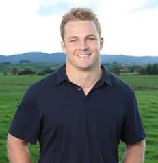 sam cane standing in front of a lush green field.