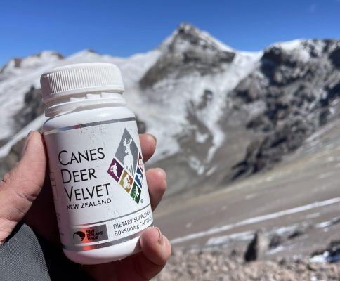 a hand holding a bottle of canes deer velvet capsules in front of the kilimanjaro mountains
