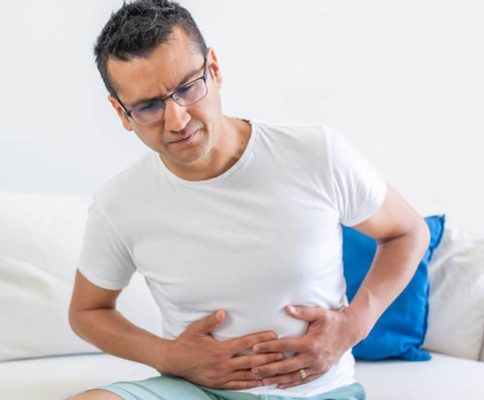 a man in a white t-shirt clutches his stomach in pain