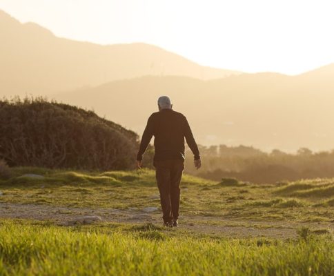 a man walking in a field with mountains in the background.