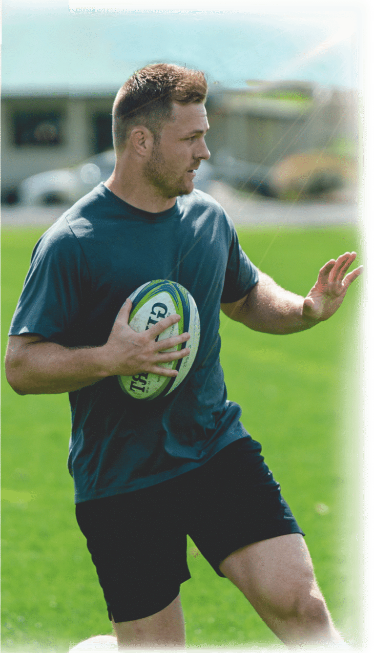 sam cane holding a rugby ball on a field fending off a defender.