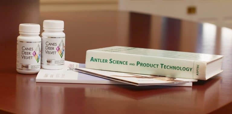 a table topped with two bottles of canes deer velvet capsules and a book titled 'antler science and product technology'.