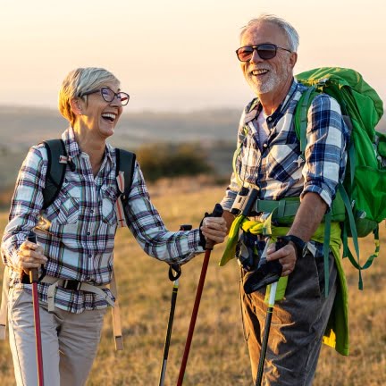 an older couple of people that are standing in the grass with packs and trail poles during a hike,