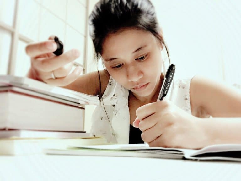 a girl is sitting at a desk with a book and a cell phone.